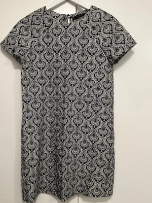 Mönstrad kortklänning från Zara - Snygg kortklänning från Zara Basic i storlek S med ett unikt, paisley-inspirerat mönster i marinblått och vitt. Klänningen har rund hals, korta ärmar och är tillverkad i ett mjukt bomullsmaterial. 