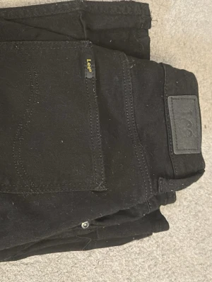 Svarta bootcut-jeans från Lee Breese - Säljer ett par svarta Lee Breese jeans med bootcut-snitt och klassisk femficksdesign. Jeansen har normal passform och är tillverkade i bomull med lite stretch för extra komfort. Snygga detaljer med Lee-logga på bakfickan och etikett i midjan.