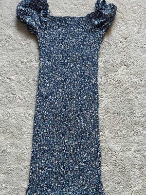 Blommig blå klänning från SHEIN - Supersöt blå kortklänning från SHEIN i storlek XS med små vita och röda blommor. Klänningen har puffiga kortärmar. Perfekt för sommarens alla tillfällen! Den är väldigt strechig vilket är bra. 