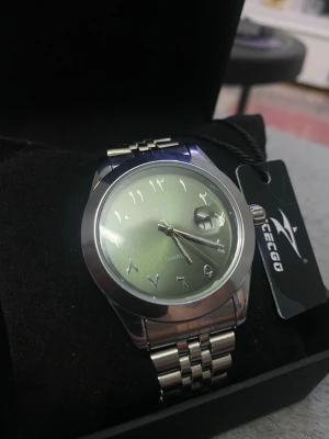 Ricecgo olivergrön klocka - Bilderna visar en klocka från Ricecgo, inte en väst. Ingen information om väst kan ges.