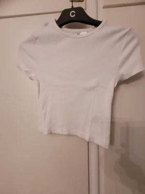 Vit croppad topp från H&M Divided - Säljer en enkel och fräsch vit croppad topp från H&M Divided. Toppen har rund hals, korta ärmar och är ribbad i materialet. Perfekt att matcha med jeans eller kjol för en clean look.