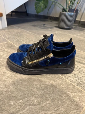 Blå sammetssneakers från Giuseppe Zanotti - Jättefina giuseppe zanotti skor som ar svarta med blåa detaljer. Kvitto finns.De blåa detaljerna är gjorda av sammet och det finns detaljer av PU-läder. De har en dragkedja och skosnören som stängning. Dragkedjan gör att även om skorna är lite för små så kan de justeras. De är jättestiliga och man kan ha dem till vardags och till speciella tillfällen. De är använda men har många år kvar att anvandas! Storlek 42,5 och de passar till alla som har storlek 42-43. Skicka gärna bud eller meddelande. 😊