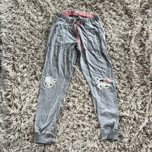 Grå mjukisbyxor med kattmotiv - Grå mjukisbyxor med söta kattansikten på knäna och texten 'All you need is me..' tryckt på ena sidan. Byxorna har rosa snörning i midjan och muddar vid bensluten.  Materialet är mjukt bomullstyg, perfekt för chill dagar hemma. Storlek XS. Från Cubus.
