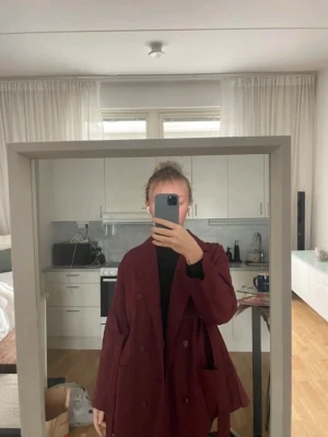 Elegant vinröd damkappa med bälte - Stilren och klassisk damkappa i vinröd färg. Passar perfekt för vår och höst. Har midjebälte som ger en fin och feminin passform. Bekväm att bära och lätt att matcha till både vardag och finare tillfällen. Mycket bra skick och välvårdad.