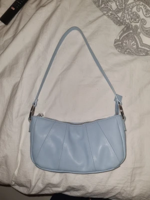 Ljusblå axelväska från Carin Wester - Säljer en ljusblå axelväska från Carin Wester i mjukt skinn. Väskan har stilrena veck på framsidan, silverfärgad dragkedja och ett rymligt fack med flera kortfickor inuti. Perfekt storlek för det viktigaste och snygg att ha över axeln.