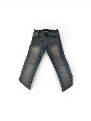 Cheap Monday blå jeans, storlek 26/32 - Snygga Cheap Monday  jeans i klassisk blå tvätt med lätt slitning på låren och raka ben. Jeansen har fem fickor, silverfärgade nitar och brunt läderpatch bak. Passformen är slim och materialet är robust denim i bomull.