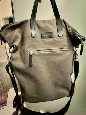 Sandqvis axelväska äldre utgåva  - Snygg washed brun/khaki axelväska från Sandqvist i slitstark canvas med svarta detaljer i skinn. Modellen som sedan lång tid inte längre produceras och är minst sagt en raritet. Väskan har både handtag och justerbar axelrem, samt en praktisk ytterficka med dragkedja framtill. Perfekt för dig som vill ha en stilren men samtid en rymlig väska till vardagen. Kapaciteten ca 18 L rymmer utan problem 16-tum laptop, böcker och träningskläder. Men plats över ;) 