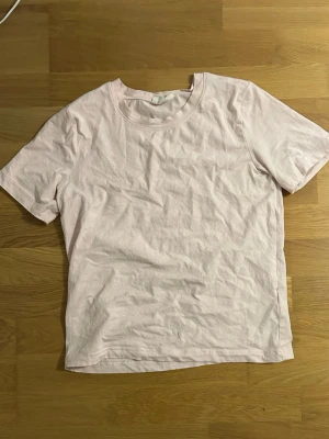 Ljusrosa t-shirt - En enkel och mjuk ljusrosa t-shirt från Gina Tricot, basically basics-kollektionen. Modellen är klassisk med rund hals och korta ärmar. Perfekt för dig som gillar stilrena och bekväma plagg. Materialet är bomull och passformen är normal. Säljer då den aldrig kommit till användning 