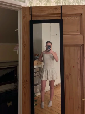 Vit kort sommarklänning med tunna ränder - Supersöt vit kort klänning med tunna vertikala ränder och smala axelband. Klänningen har en figurnära överdel och en lätt utställd kjol med vågig kant. Perfekt för varma dagar och ger en fräsch och ungdomlig look. Fråga mig om ni undrar något 😊