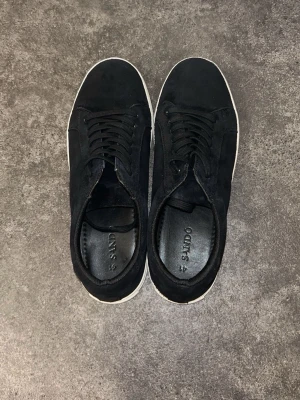Svarta sneakers från SAND - Svarta sneakers från SAND med vit platt sula och klassisk rund tå. Skorna har snörning och är tillverkade i mocka med en stilren och enkel design. Perfekta för dig som gillar minimalistisk stil och vill ha ett par snygga sneakers med skön passform.