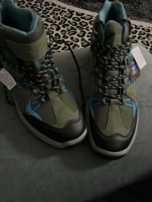 Gröna kängor från Crivit strl 39 - Säljer ett par gröna kängor från Crivit med svarta och blå detaljer. Skorna har grov sula för bra grepp, snörning och blått innerfoder. Materialmix av syntet och textil, perfekta för utomhusaktiviteter. Snygg outdoor-look med coola kontrastdetaljer.