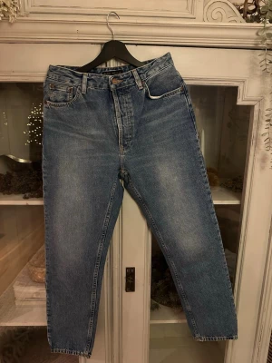 Blå jeans från Nudie Jeans Co, ny med tag kvar  - Säljer ett par klassiska blå jeans från Nudie Jeans Co med snygga kontrastsömmar och broderade bakfickor. Jeansen har normal passform, raka ben och är tillverkade av ekologisk eller återvunnen bomull. Perfekt för dig som gillar tidlös stil och schyssta material.