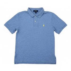 Blå pikétröja från Polo Ralph Lauren - Säljer en klassisk blå pikétröja från Polo Ralph Lauren med korta ärmar och krage. Tröjan har två knappar framtill och en gul broderad logga på bröstet. Perfekt för en chill och stilren look.  (Storlek junior M (10-12)