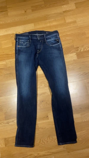 Replay Anbass Hyperflex jeans blå 29 - Säljer ett par Replay Anbass Hyperflex jeans i mörkblå tvätt. Klassisk femficksmodell med snygga kontrastsömmar och stretchigt material för extra komfort. Passformen är slim och modellen har normal midja. Perfekta jeans för dig som gillar stilrena och bekväma byxor.