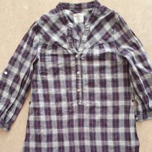 Skjortklänning - Rutig skjortklänning från H&M i blått, vitt och rött. Klänningen har knappar framtill, trekvartsärmar med knappdetalj och volang nertill. Tillverkad i mjuk bomull, perfekt för en avslappnad och cool look.