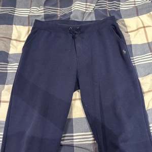 Mörkblå mjukisbyxor Polo Ralph Lauren - Snygga mörkblå mjukisbyxor från Polo Ralph Lauren med klassisk logga broderad vid fickan. Byxorna har snörning i midjan, sidofickor och en bakficka. Perfekta för chill eller träning, tillverkade i mjukt bomullsmaterial.