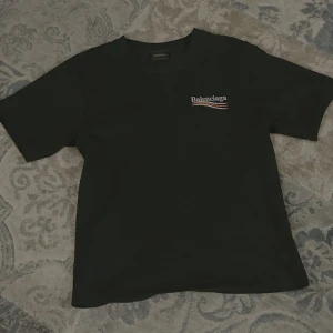 Svart  t-shirt med tryck - Svart t-shirt  med stort vitt logotryck och röda samt vita vågiga linjer på ryggen. Mindre logga med samma design på bröstet. Klassisk passform och rund halsringning. Tillverkad i mjuk bomull, perfekt för en clean och trendig look.