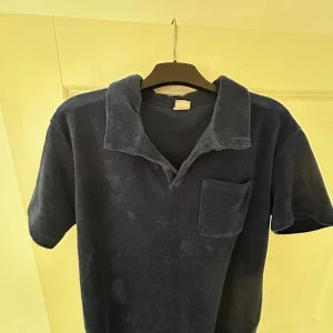 Mörkblå frotté pikétröja Lindex - Säljer en mörkblå pikétröja från Lindex i frottématerial. Tröjan har korta ärmar, klassisk krage och en bröstficka. Perfekt för dig som gillar chill och mjuka material. Passar dig som vill ha en enkel och stilren look.