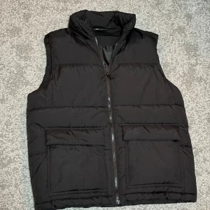 Svart dunväst   - Säljer en riktigt skön svart dunväst från Lager i storlek S, i nyskick med hög krage och två  fickor framtill. Västen har quiltad design och stängs med dragkedja. Perfekt för lager-på-lager och enkel att matcha med olika outfits.