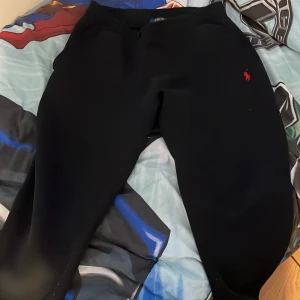 Svarta mjukisbyxor Polo Ralph Lauren - Svarta mjukisbyxor från Polo Ralph Lauren med klassisk röd broderad logga på benet. Byxorna har en bekväm passform och är gjorda i mjukt bomullsmaterial. Perfekta för chill dagar och har elastisk midja för extra komfort.