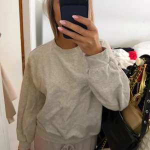 Ljusgrå sweatshirt med ballongärmar - Enkel och stilren ljusgrå sweatshirt med rund hals och ballongärmar. Tröjan har ribbade muddar vid ärmslut och midja för en skön och avslappnad passform. Perfekt för en chill och casual look.