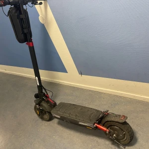 Elscooter - Kraftfull elscooter med robusta däck och stötdämpare fram och bak. Utrustad med display och förvaringsväska på styret. Synligt bruksslitage på fotplattan och bakskärmen, men i gott skick och redo för nya äventyr. 