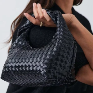 Svart flätad handväska i skinn - Snygg svart handväska med flätad design och mjuk, rundad form. Väskan har ett kort handtag som gör den enkel att bära i handen eller över armen. Materialet är skinn och ger en lyxig känsla. 