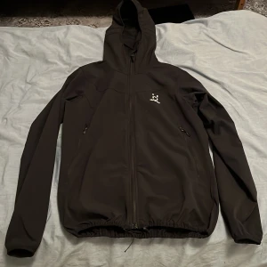 Svart vindjacka från Haglöfs med huva - Svart vindjacka från Haglöfs med hel dragkedja, huva och två sidofickor med dragkedja. 