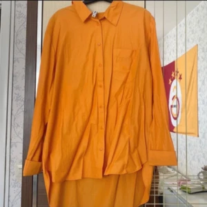 Orange skjorta från FB Sisser XL - Snygg orange skjorta från FB Sisser i storlek XL. Skjortan har klassisk krage, lång ärm med manschett, bröstficka och knappar framtill. Passformen är loose och materialet känns som bomull, perfekt för dig som gillar färgstarka plagg.