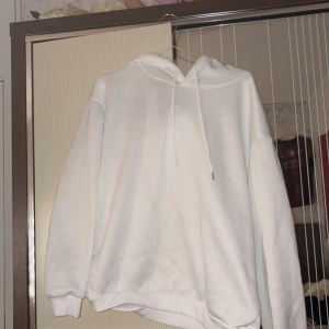 Vit hoodie med snörning - Vit hoodie med huva och snörning, tillverkad i mjukt material. Tröjan har ribbade muddar vid ärmslut och en relaxed passform. Perfekt för chill dagar och enkel att matcha med jeans eller mjukisbyxor.