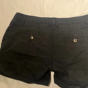 Svarta cargoshorts - Snygga svarta cargo shorts med klassisk design och uppvikta benslut. De har två fickor med knappstängning bak och sidofickor fram, samt hällor för bälte. Super söta och ger en y2k vibe💕🪩✨