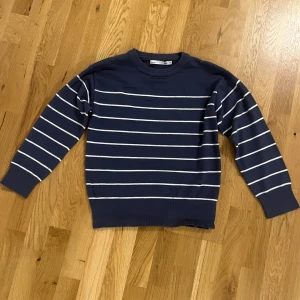 Marinblå randig tröja från 157 - Snygg marinblå tröja med vita horisontella ränder från 157. Rund hals och långa ärmar med ribbade muddar. Perfekt för dig som gillar klassisk stil.