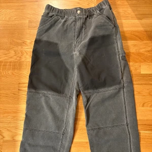 Grå cargopants med svarta förstärkningar - Säljer ett par grå cargopants från Zara med svarta förstärkningar på knäna. Byxorna har flera fickor, elastisk midja och robusta sömmar. Perfekta för dig som gillar funktionella och slitstarka byxor med cool arbetsstil.