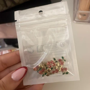 Små nageldekorationer i körsbärsdesign - Säljer ett gäng söta dekorationer med körsbärsdesign. De har glittriga röda stenar som bär och gröna blad i metall, med guldfärgade detaljer. 