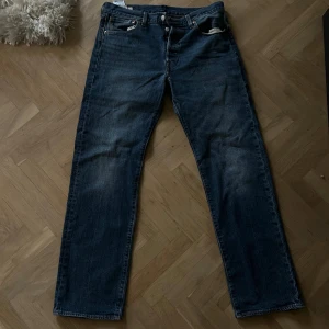 Levi's 501 jeans blå W33 L32 - Klassiska Levi's 501 jeans i mörkblå denim med raka ben och fem fickor. Snyggt slitna detaljer och ikonisk läderpatch bak i midjan. Passar dig som gillar tidlös stil och vill ha ett par jeans med autentisk känsla.