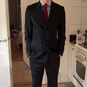 Mörkblå kostym från Douglas Hayward -  Marinblå kostym från Douglas Hayward Mayfair London, tillverkad i 100% fin italiensk ull. Kavajen är dubbelknäppt med klassisk krage och flera fickor, byxorna har raka ben och bälteshällor. Kavajen är använd en gång men byxorna är aldrig använda, lapparna finns kvar på dem. 