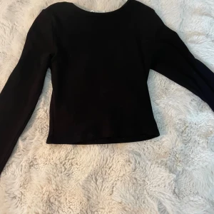 Svart ribbad långärmad topp från DIVIDED - Säljer en svart långärmad topp från DIVIDED i storlek XXS. Toppen är ribbad och har en enkel, rund halsringning. Perfekt att styla med jeans eller kjol för en clean look. Materialet är mjukt och stretchigt, vilket gör den skön att bära hela dagen.