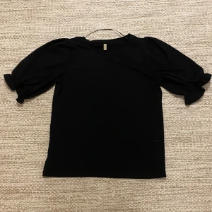 Svart blus med puffärm från Soyaconcept/åhlens - Svart blus från Soyaconcept i storlek M. Modellen har puffiga korta ärmar med rynkade detaljer och rund halsringning. Materialet är mjukt och lätt, perfekt för en chill och stilren look. Snygg att matcha med jeans eller kjol för en trendig vibe.