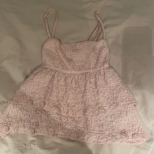 Ljusrosa volangtop från Gina Tricot - Supersöt ljusrosa topp från Gina Tricot i storlek S. Toppen har smala axelband, volangdetaljer och ett smockat, krinklat tyg som ger en fluffig och luftig känsla. Nästan aldrig använd