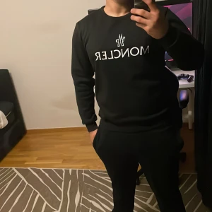 Svart Moncler sweatshirt med logga - Svart sweatshirt  Moncler med vit logotyp tryckt på bröstet. Tröjan har rund hals, långa ärmar och ribbade muddar vid ärmslut och nederkant. Stilren och enkel design som passar perfekt till streetwear. Materialet känns mjukt och skönt mot huden.
