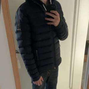 Mörkblå dunjacka Parajumpers - Snygg mörkblå dunjacka från Parajumpers med orange innerfoder. Jackan har två dragkedjeförsedda fickor, hög krage och klassisk logga på ärmen. Perfekt för kyliga dagar och har en stilren, sportig look.