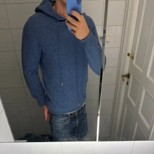 Blå merino hoodie - Mysig blå hoodie i kashmir. Tröjan har en enkel och stilren design, perfekt för dig som gillar en avslappnad men ändå snygg look. Passformen är normal och materialet känns riktigt lyxigt och mjukt mot huden.
