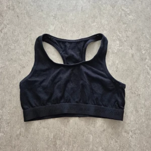 Sport-bh - Svart sportig sport-bh från KappAhl med bred resår nertill där det står 'BODY ZONE'. Modellen har brottarrygg och är tillverkad i mjuk bomull som känns skön mot huden. Perfekt för träning eller chill dagar.