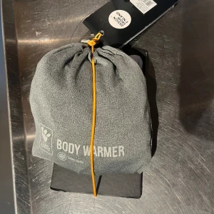 Grå Body Warmer från Hurtta 45XS - Body Warmer från Hurtta i grått, designad för hundar. Jackan är helkroppstäckande med hög krage och långa ben, tillverkad i mjukt syntetmaterial som reflekterar kroppsvärme. Perfekt för kalla dagar och extra värme till din hund. Endast testad