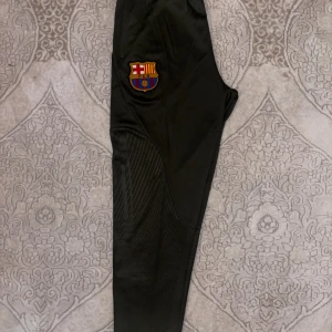 Barcelona träningsbyxor från Nike - Helt nya mörkgröna FC Barcelona  träningsbyxor från Nike . Byxorna är oanvända och taggarna sitter kvar, har dragkedja vid fickorna och är gjorda i ett syntetmaterial som andas. Smal passform och elastisk midja för skön känsla.