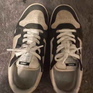 Svarta och vita sneakers från Axel Arigato - Snygga sneakers från Axel Arigato i svart och vitt med coola kontraster och klassisk siluett. Skorna har snörning, rund tå och platt sula. Tillverkade i Portugal med ovandel i mocka och textil. Perfekta för dig som gillar streetstyle och vill ha något unikt.