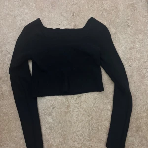 Svart croppad långärmad topp - Säljer en svart croppad topp med lång ärm och fyrkantig halsringning. Toppen är ribbad och har en tight passform som framhäver siluetten. Perfekt att styla med höga jeans eller kjol för en trendig look. Aldrig använd för kort i min smak