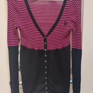 Randig kofta från ONLY, svart/rosa - Snygg kofta från ONLY i svart och rosa med smala ränder upptill och enfärgad svart nedtill. V-ringad med knappar hela vägen och långärmad. Stickad i mjukt material och så fin passform. Den är oanvänd så I nyskick.                                  Från rök och djurfritt hem.