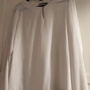 Vit blus med knappdetaljer - Säljer en stilren vit blus från Åhlens i storlek M. Blusen har långärmade ärmar med knapp vid manschetten och en snygg knappöppning vid halsen. Materialet är mjukt och lätt, perfekt för dig som gillar en clean look. Passar dig som vill ha en enkel men elegant topp.