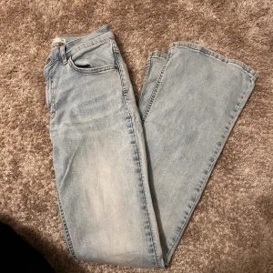 Ljusblå bootcut jeans från Gina tricot - Säljer ett par ljusblå jeans från Gina tricot med klassisk femficksdesign och utsvängda ben. Jeansen har medel midja och är tillverkade i bomull med en mjuk jeanskänsla. Perfekt för dig som gillar en avslappnad och stilren look.